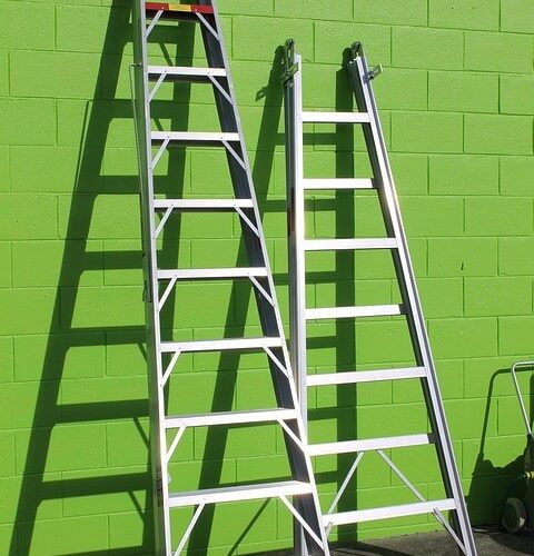 two ladders leaning on a green wall